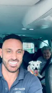 Pets 2 Places pet taxi driver smiling with an elderly customer and her small white dog during a pet-friendly journey.