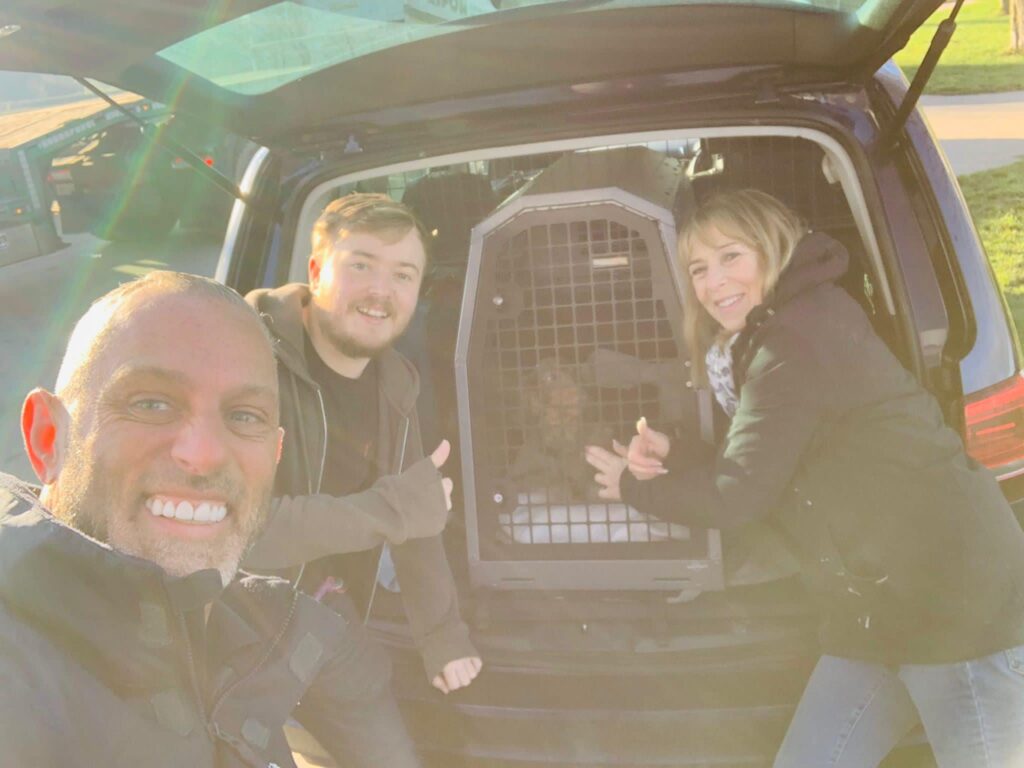 franchisee taking selfie with two customers and their dog safely in crate in boot of car